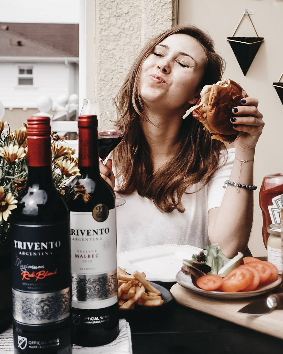 A lady sitting on a chair with a table set with food and a bottle of wine