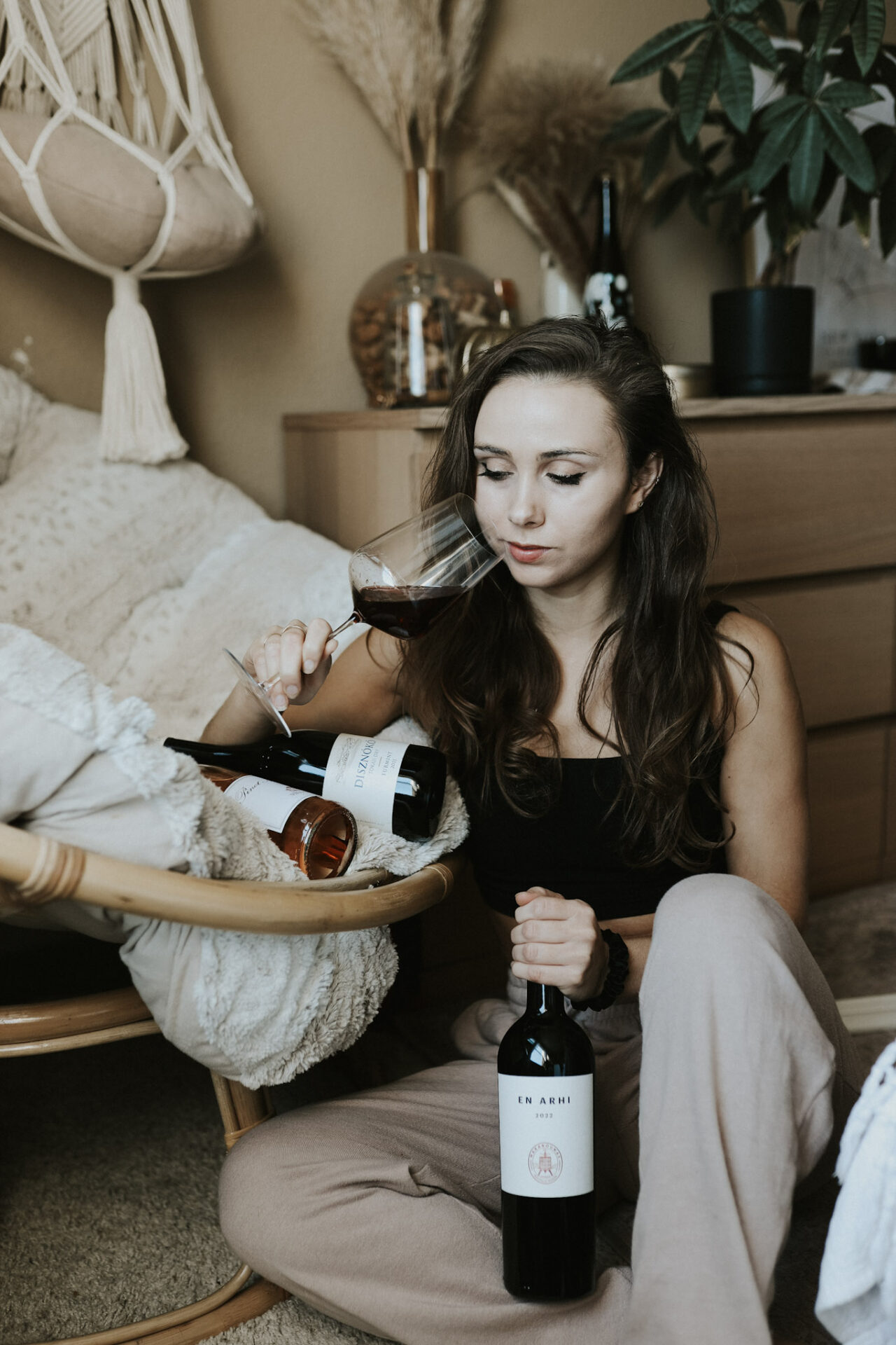 Paige sipping a glass of red wine on the floor with three bottles of EU wines around her