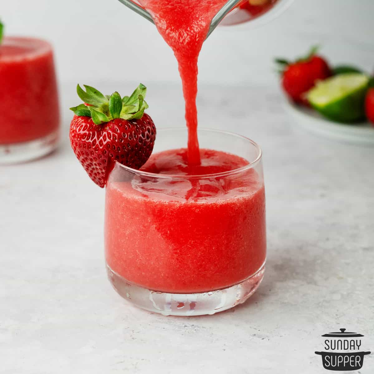 Strawberry Daiquiri Sweet Cocktails being poured into a short glass and strawberry by the side