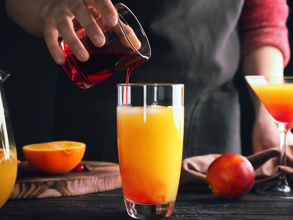 low calorie tequila sunrise drink in a glass with a hand holding a glass and pouring into it