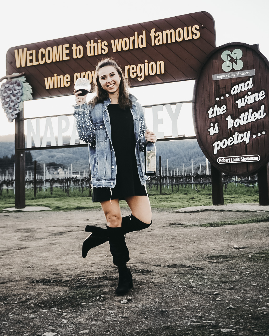 California Wine History-A lady holding a wine glass in front of the "Welcome to Napa" sign in Napa, CA