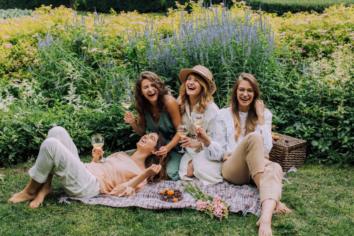 Girls on a picnic blanket laughing with wine